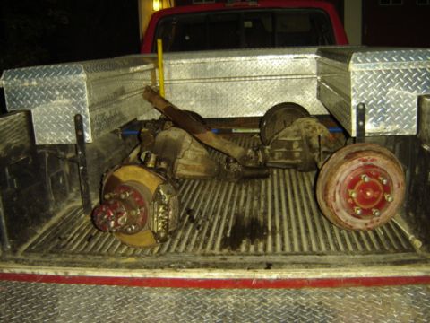 1992 Ford Bronco - Two axles and brake components are loaded into the bed of a red pickup truck.