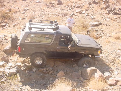 1988 Ford Bronco - A black 1988 Ford Bronco is shown off-roading over rocks in a desert landscape.