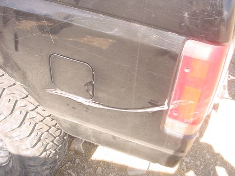 1988 Ford Bronco - The rear quarter panel of a black 1988 Ford Bronco shows significant scratches and a dent near the gas cap door.