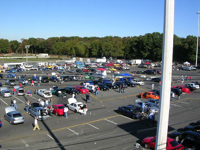 Cars parked in a lot with trees and a white pole in the foreground