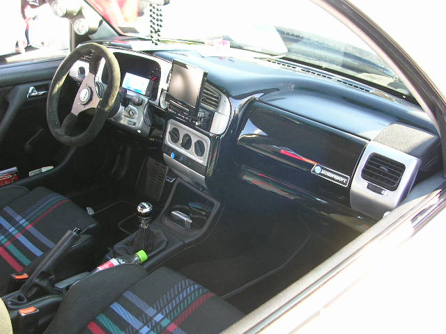 Car interior with plaid seats, aftermarket steering wheel, and a modern infotainment screen