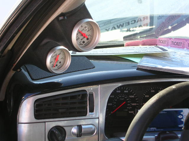 Dashboard with two aftermarket gauges, air vent, and speedometer. Tickets are on the windshield