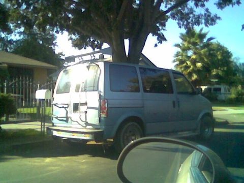 1998 Mercury Sable - A blue van is parked under a large tree on a sunny day, with another van in the distance.