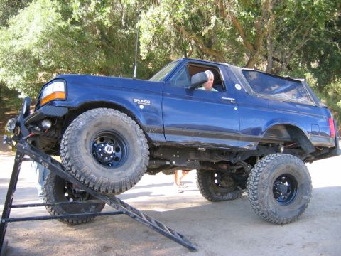 1985 Ford Bronco - A blue Ford Bronco is shown on a ramp, demonstrating its off-road capabilities.