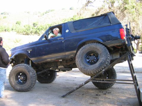 1985 Ford Bronco - A blue Ford Bronco is shown on a ramp, with a woman in the driver's seat and a man standing beside it.