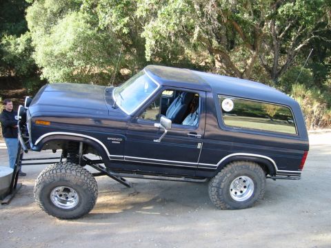 1985 Ford Bronco - A lifted Ford Bronco with custom suspension sits on a dirt road.
