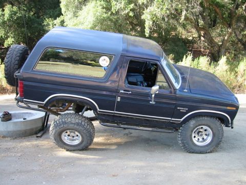 1985 Ford Bronco - This 1985 Ford Bronco features a lifted suspension and large off-road tires, suggesting it's prepared for terrain.