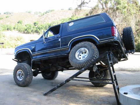 1985 Ford Bronco - Blue Ford Bronco on a ramp, showing its lifted suspension and off-road tires.