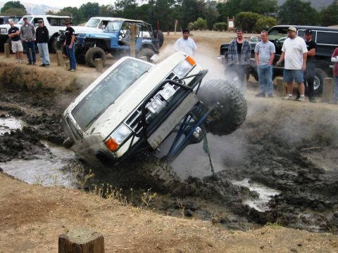 1985 Ford Bronco - An off-road vehicle is stuck in a mud pit while spectators watch.