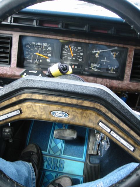 1985 Ford Bronco - The dashboard of a 1980s Ford Bronco, wood-grain accents and branded floor mats.