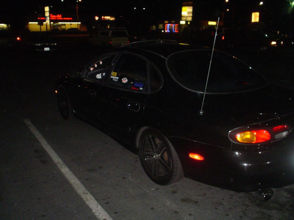black sedan parked at night, antenna on roof, stickers on window
