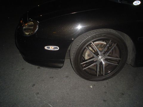 1993 Ford Taurus - Close-up of a black car's front fender and wheel, aftermarket rims and a clear turn signal.
