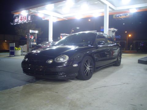 1993 Ford Taurus - A black sedan is parked at a gas station under bright lights at night.