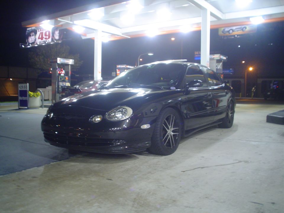 Black sedan parked at a gas station at night, front 3/4 view