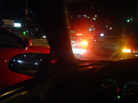 1993 Ford Taurus - Nighttime interior view from a car, with a red vehicle visible to the left and dashboard gauges illuminated.