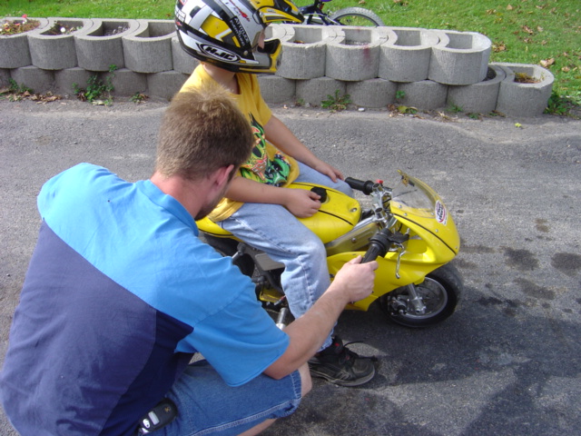 Yellow pocket bike with child rider and adult assisting
