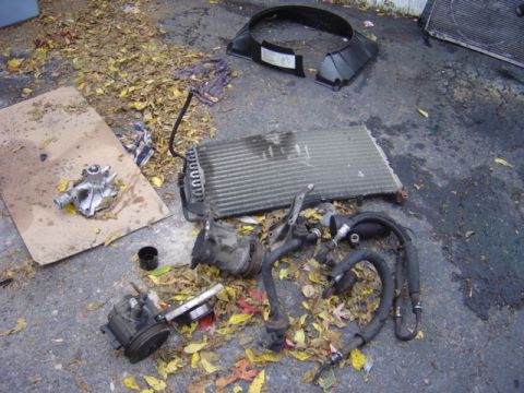 1998 Ford Taurus - Disassembled car parts like a radiator and water pump are laid out on the ground.