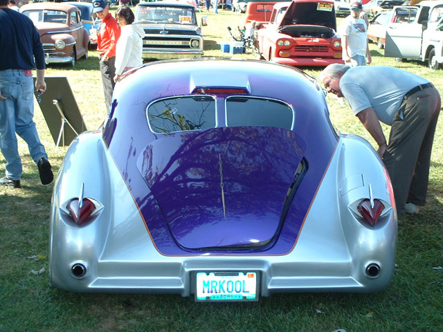 Custom hot rod with purple and silver paint, MRKOOL license plate. Other cars and people in background