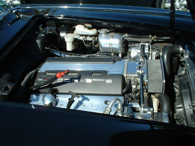 Close-up of a black car's engine bay, showing a 'CORVETTE' branded engine cover and various engine components