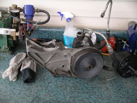 1996 Ford Bronco - A power steering pump assembly is shown with associated parts and tools on a workbench.