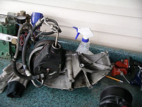 1996 Ford Bronco - A power steering pump assembly, likely removed for repair or replacement, sits on a workbench with various tools and supplies.