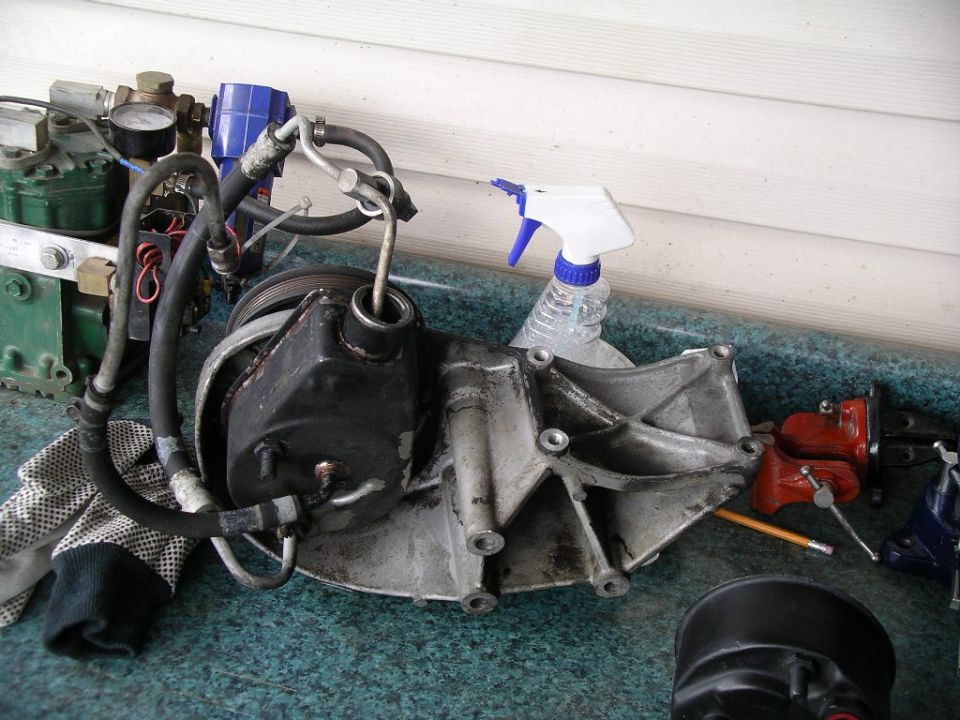 Greasy power steering pump and bracket with hoses and pulley on green surface