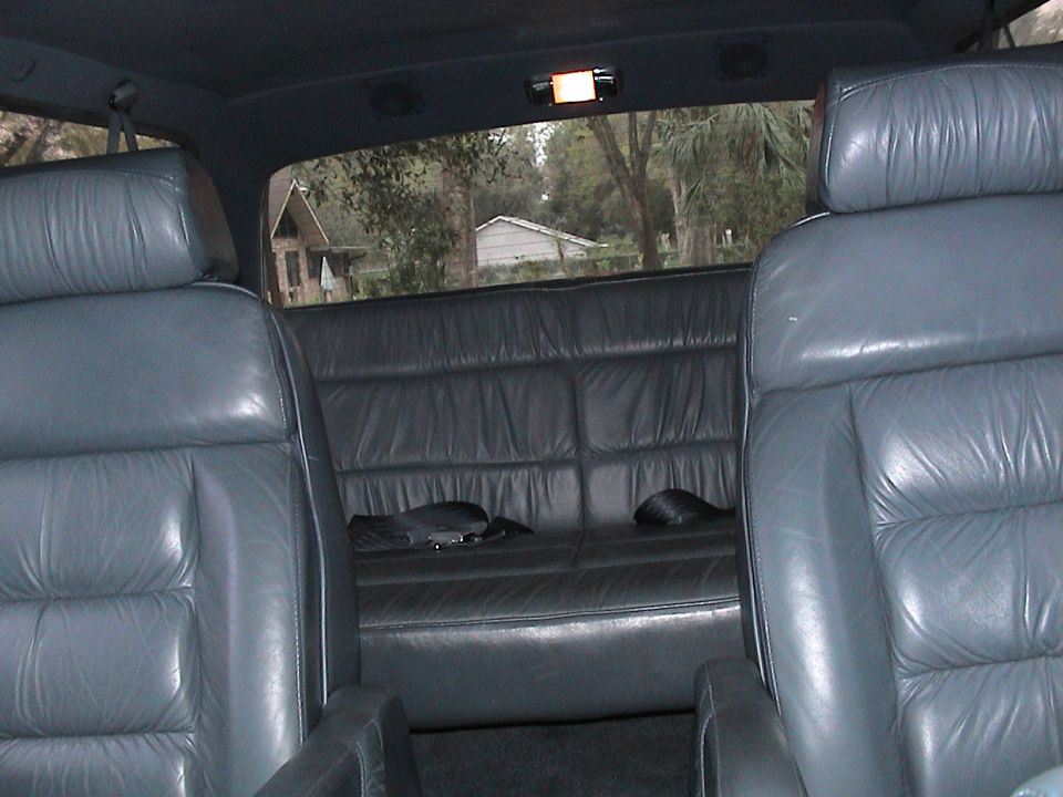 Gray leather rear seats and folded-down bench inside an SUV, looking out the back glass at trees