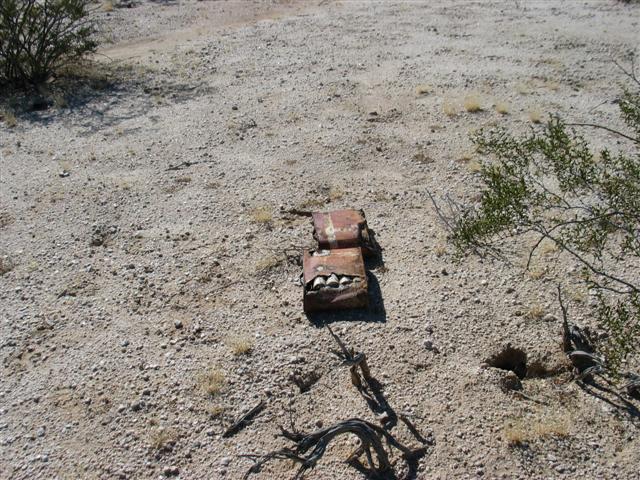 Rusty red metal fuel can torn open, lying on desert gravel among dry brush