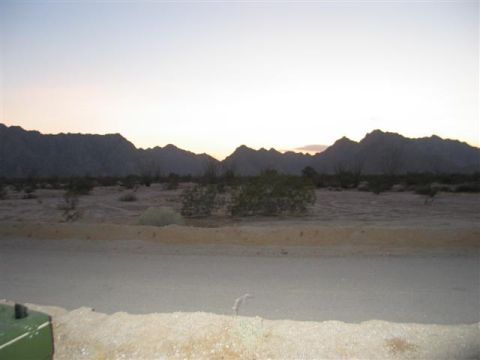 1994 Ford Bronco - A desert landscape with mountains silhouetted against a dusky sky. Part of a green vehicle is visible in the lower left corner.