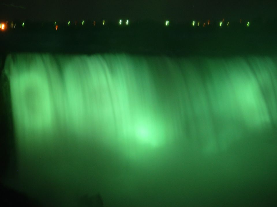 Niagara Falls illuminated green at night with lights visible in the distance