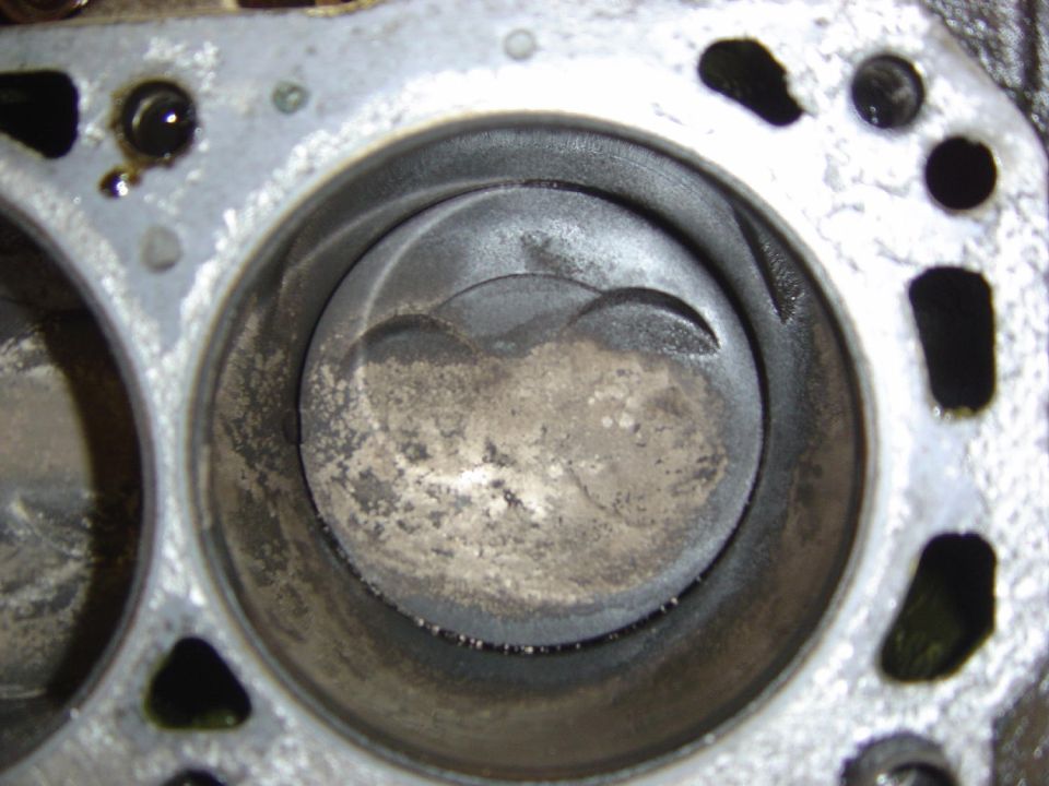 Engine block with two cylinders and pistons visible, showing wear and carbon buildup