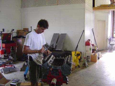1993 Ford Bronco - A mechanic works on an engine block in a cluttered garage with tools and parts scattered around.