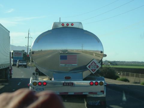 1989 Ford Bronco - A tanker truck with an American flag decal and 'HEIL' branding is seen on the highway, reflecting the surrounding landscape.