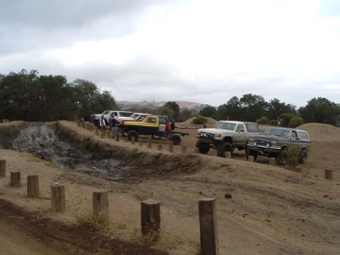 1989 Ford Bronco - Group of off-road vehicles gathered at a dirt track, including a 1989 Ford Bronco.