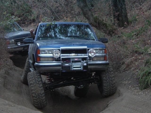 Dark blue lifted Ford Bronco with winch flexing through a rutted dirt trail
