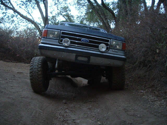 Lifted dark blue Ford 4x4 flexing on a dirt trail at dusk with grille-mounted lights