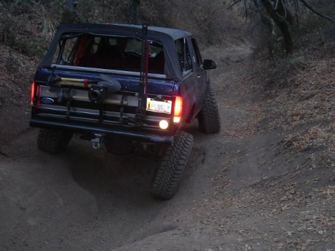 1989 Ford Bronco - This SUV, likely from the 1980s, is seen from the rear on a dirt trail, equipped for off-road use.