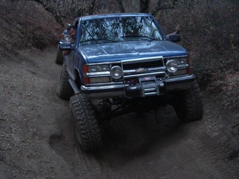 1989 Ford Bronco - A blue pickup truck navigates a dirt trail, equipped with a winch for off-road adventures. The vehicle appears to be from the early 1990s.