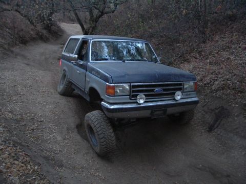 1989 Ford Bronco - This Ford Bronco is navigating a steep, dirt path with trees in the background.