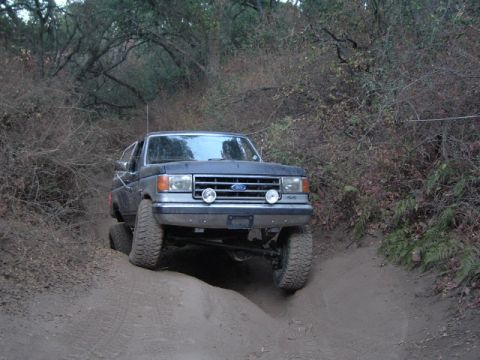 1989 Ford Bronco - A dark blue Ford Bronco navigates a challenging dirt trail with steep inclines.
