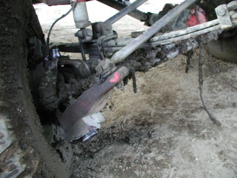 1993 Ford Bronco - Close-up of a heavily mud-caked vehicle suspension system, showing leaf springs and a shock absorber.