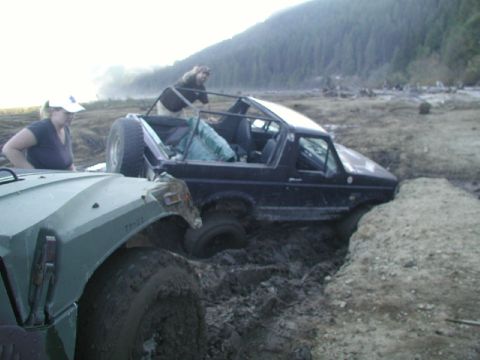 1993 Ford Bronco - Two vehicles are stuck in a muddy terrain with people around them.