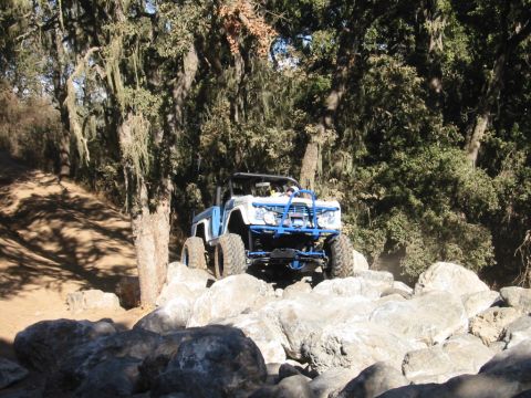 1985 Ford Bronco - An off-road vehicle tackles a challenging rocky path surrounded by trees.