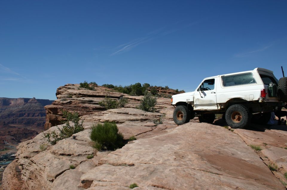 White Ford Bronco parked on a flat slickrock ledge above a deep desert canyon under blue sky