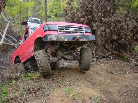 1983 Ford Bronco - Red Ford F-Series truck is stuck on a muddy incline with another white truck behind it.
