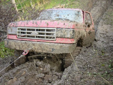 1983 Ford Bronco - This mud-covered Ford Bronco appears to be from the early 1980s, not 1983, and is deeply stuck in a muddy off-road trail.