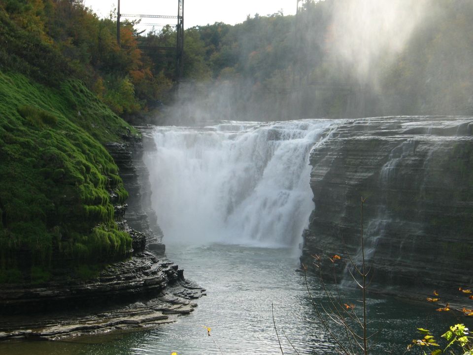 Waterfall cascading over layered rocks with mossy green cliffs and trees in the background