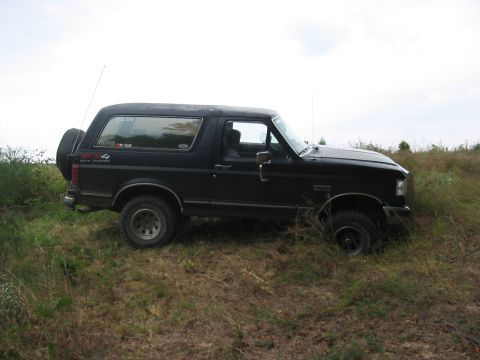 1988 Ford Bronco - A black 1988 Ford Bronco is seen parked on a grassy incline, with its spare tire mounted on the rear.