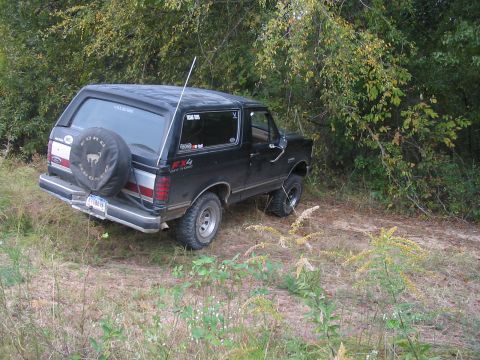 1988 Ford Bronco - This black Ford Bronco is parked off-road, with a spare tire mounted on the back and "FX4 OFF ROAD" badging visible.