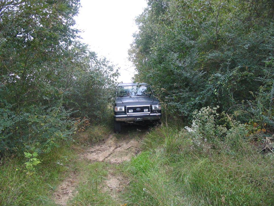 1988 Ford Bronco driving on a dirt path through trees